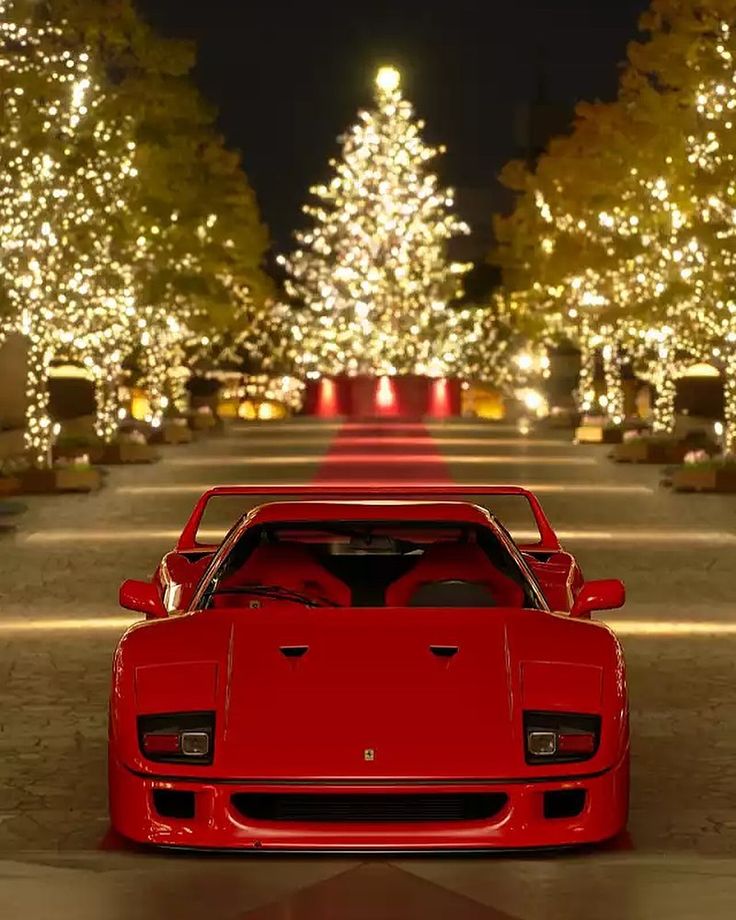 a red sports car parked in front of a christmas tree with lights on the trees