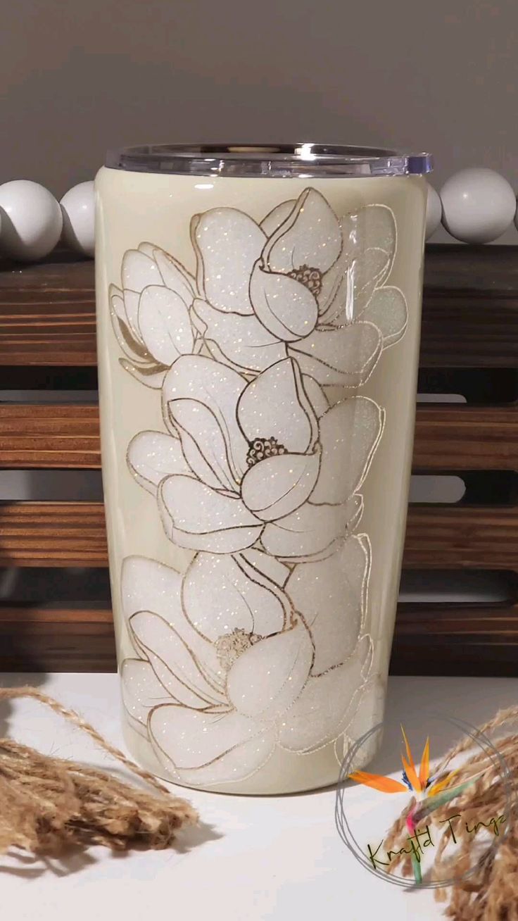 a white glass with flowers on it sitting next to some brown and white balls in the background