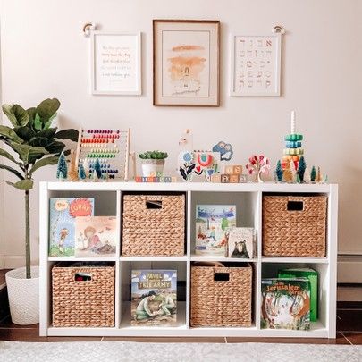 a white shelf filled with lots of books and toys next to a potted plant