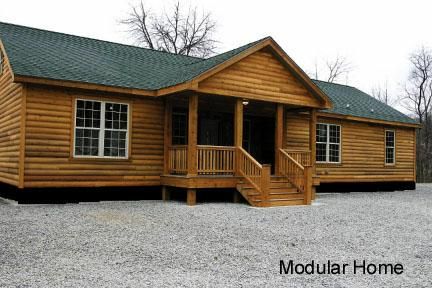 a large log cabin sits in the middle of a gravel lot with stairs leading up to it