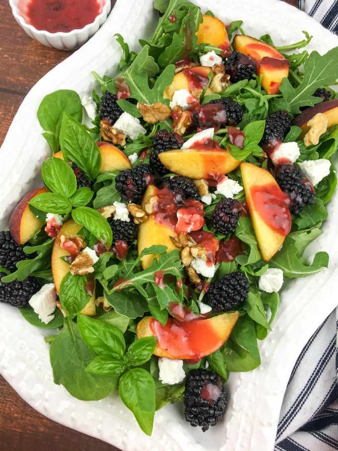 a salad with peaches, spinach and blackberries on a white platter