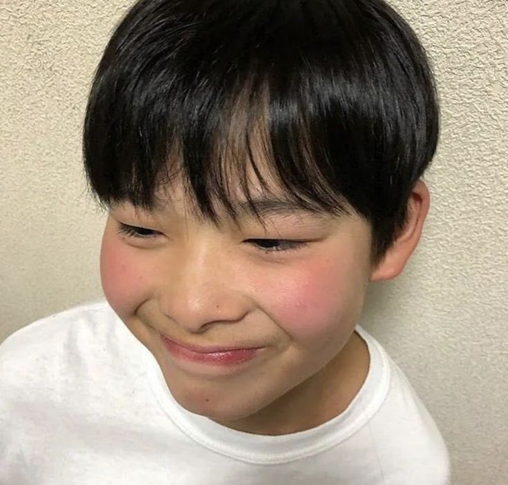 a young boy with black hair smiling at the camera