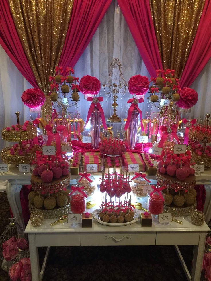 a table topped with lots of desserts covered in pink and gold decorations on top of it