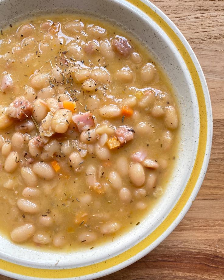 a bowl filled with beans and ham on top of a wooden table