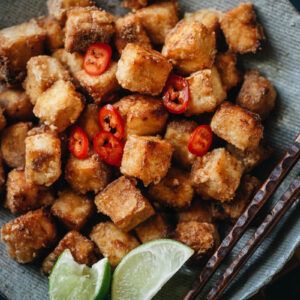 fried tofu with tomatoes and limes in a bowl next to chopsticks