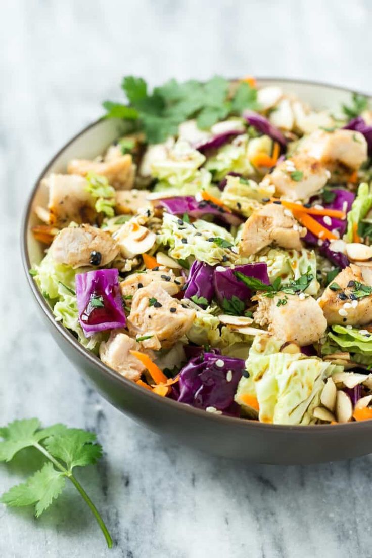 a salad with chicken, lettuce and carrots in a bowl on a marble surface