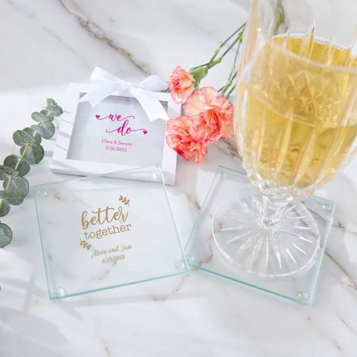 two glass coasters sitting next to each other on a marble surface with flowers in the background