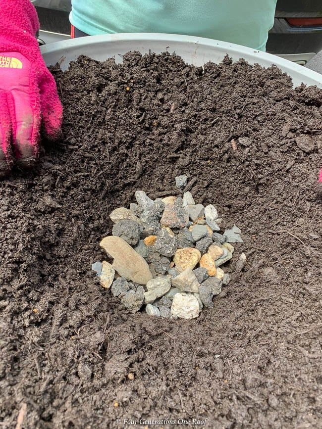 a bucket filled with dirt and rocks next to a person's hand in pink gloves