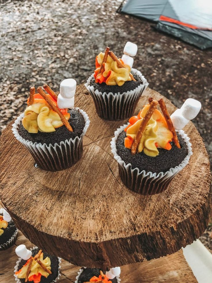 cupcakes with marshmallows and toppings on a tree stump