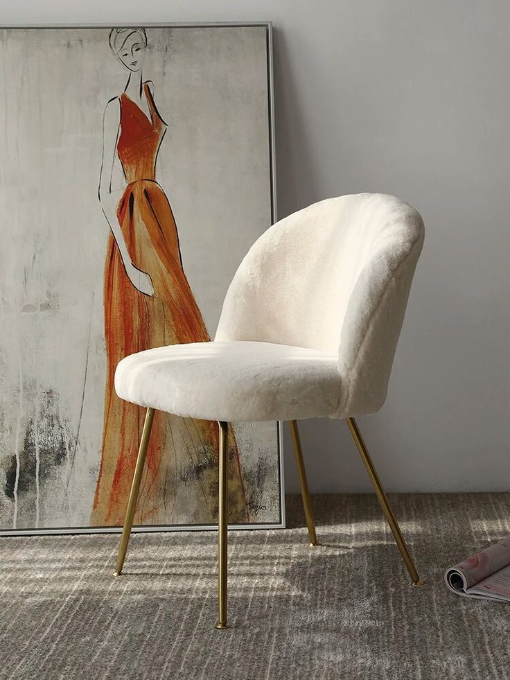 a white chair sitting in front of a painting on the wall next to a pair of shoes