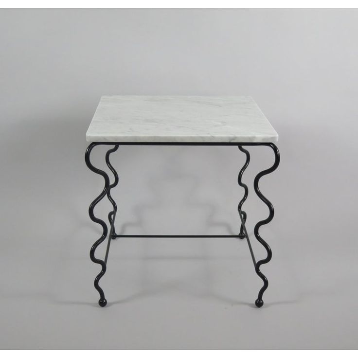 a white marble top table with black metal legs and an intricate design on the base