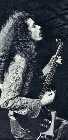 an old black and white photo of a man with long hair holding a guitar in his right hand