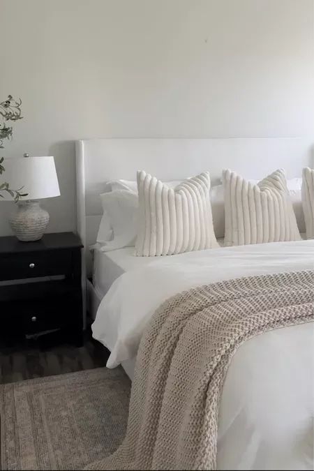 a bed with white sheets and pillows on top of it next to a night stand