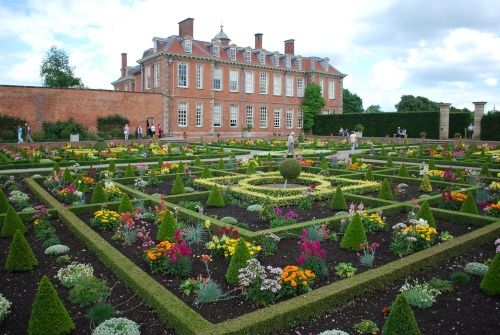 an elaborate garden in front of a large brick building with many flowers and bushes around it