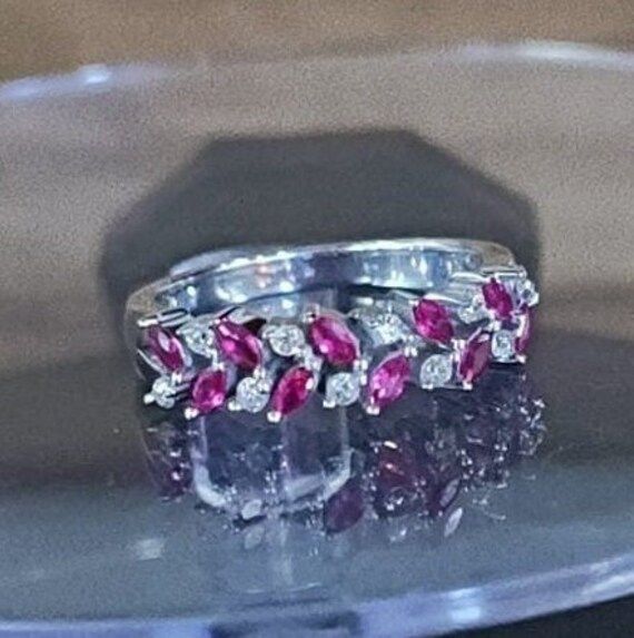 two wedding rings with pink and white stones on top of a clear plate in front of a black background