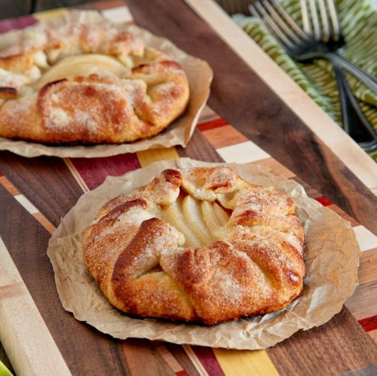 two apple pies sitting on top of a wooden cutting board next to each other