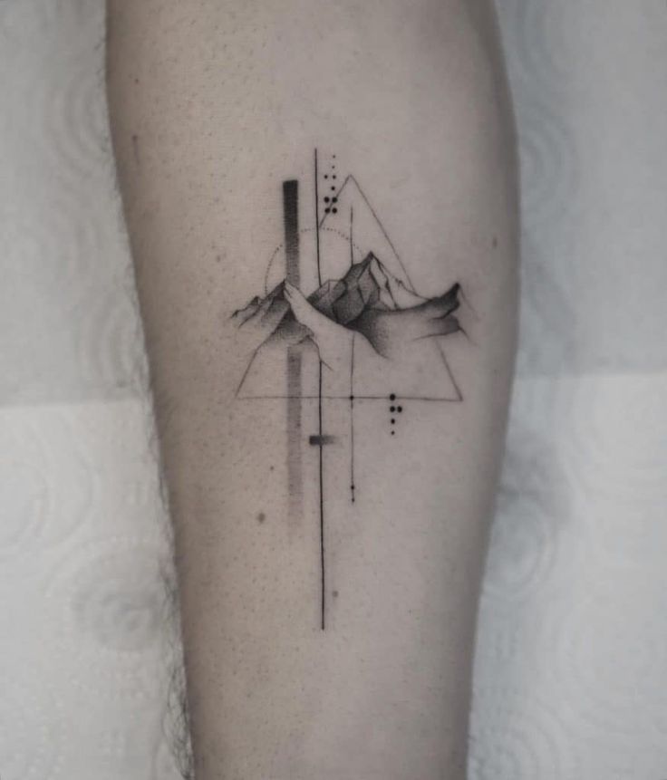 a black and white tattoo on the leg of a person with mountains in the background