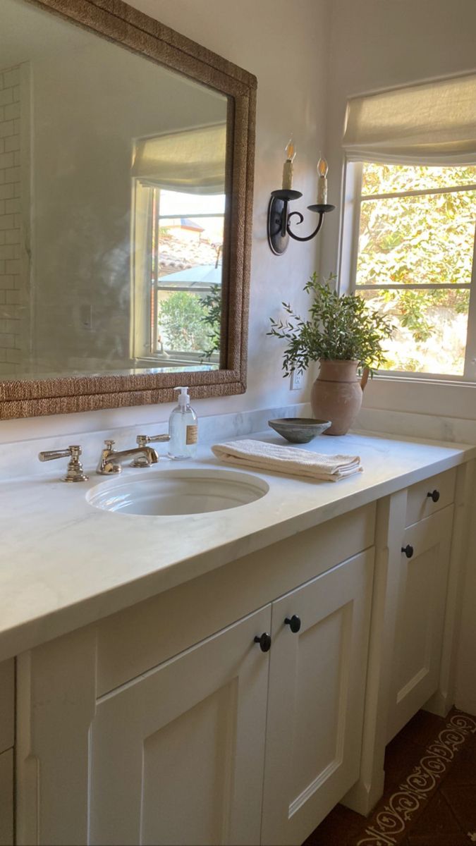 a bathroom sink with a large mirror above it and a vase on the counter top