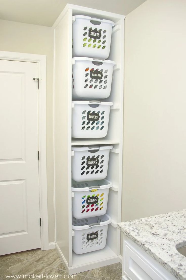 a white shelf filled with plastic baskets next to a marble counter top in a bathroom