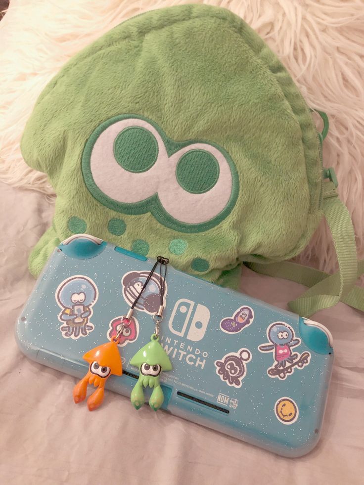 a green stuffed animal next to a nintendo wii game case and keychain on a bed