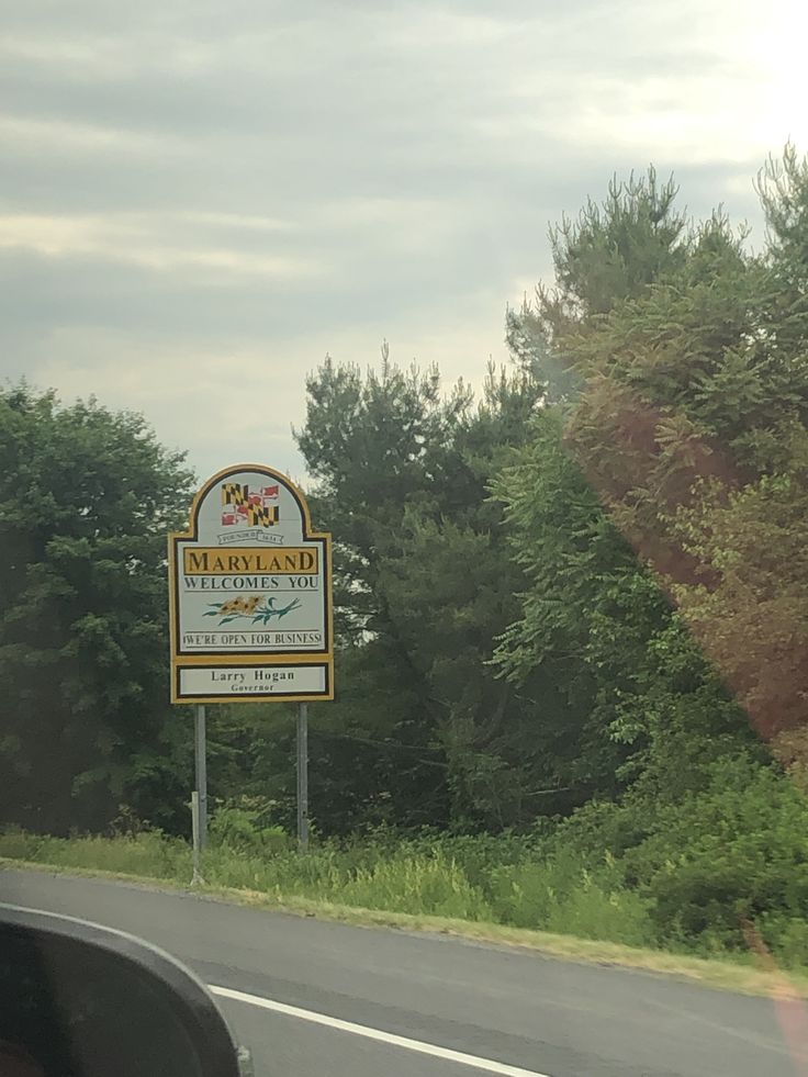 a sign on the side of a road in front of some trees and bushes,