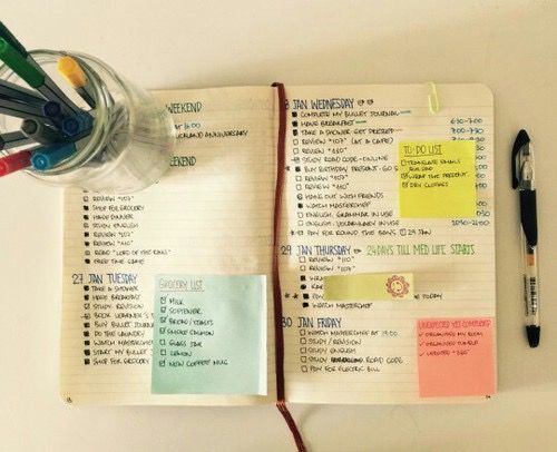 an open notebook with notes, pens and markers on it next to a cup of water