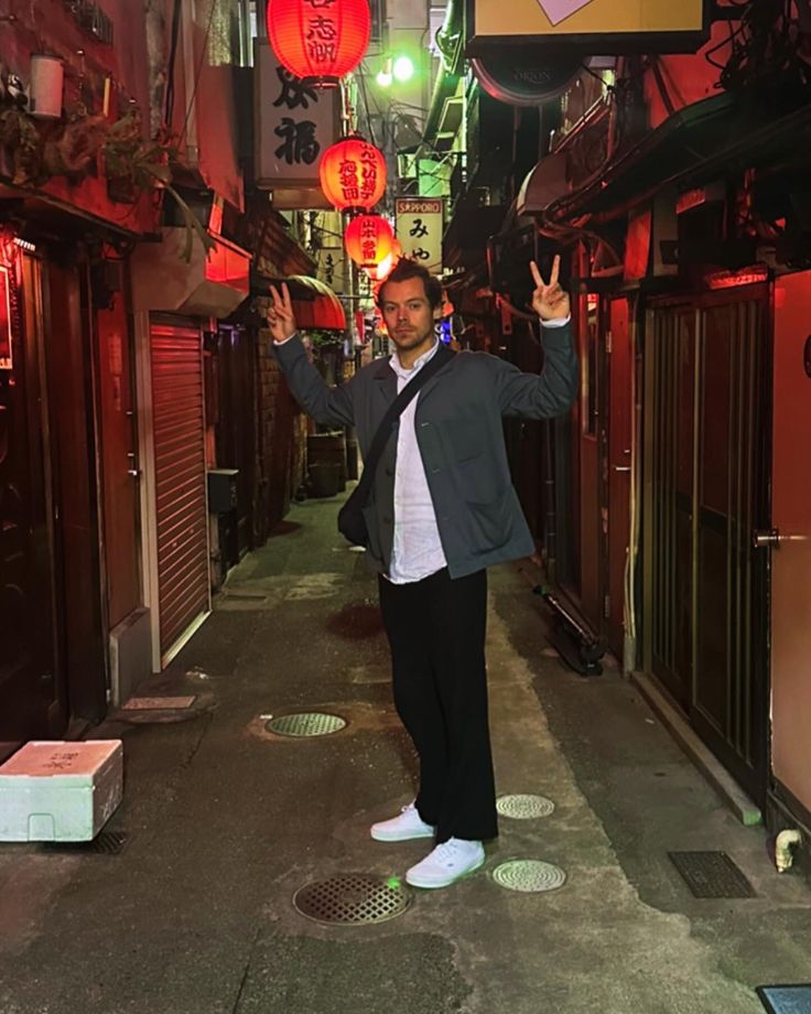 a man standing in an alley way with his arms up and two red lanterns hanging from the ceiling