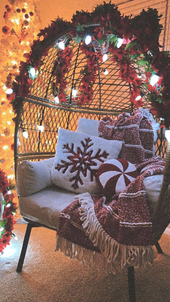 a chair with pillows and blankets on it in front of a christmas tree decorated with lights