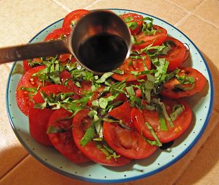 a blue and white plate topped with sliced tomatoes next to a metal spoon on top of a tile floor