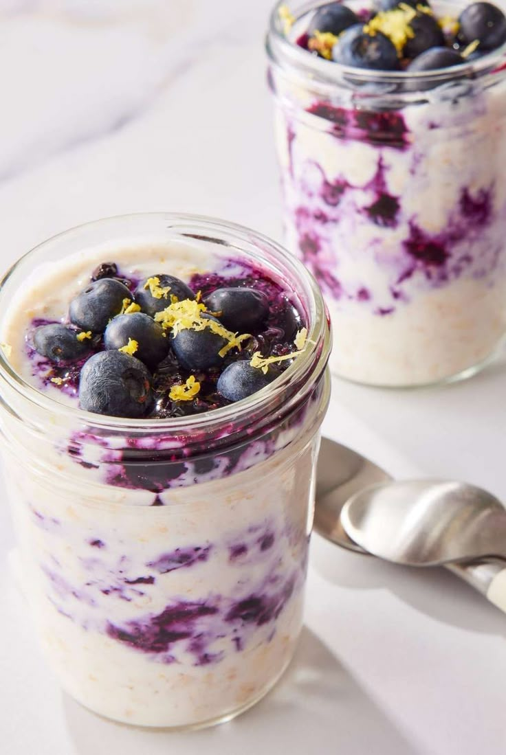 two jars filled with yogurt and blueberries on top of a white table