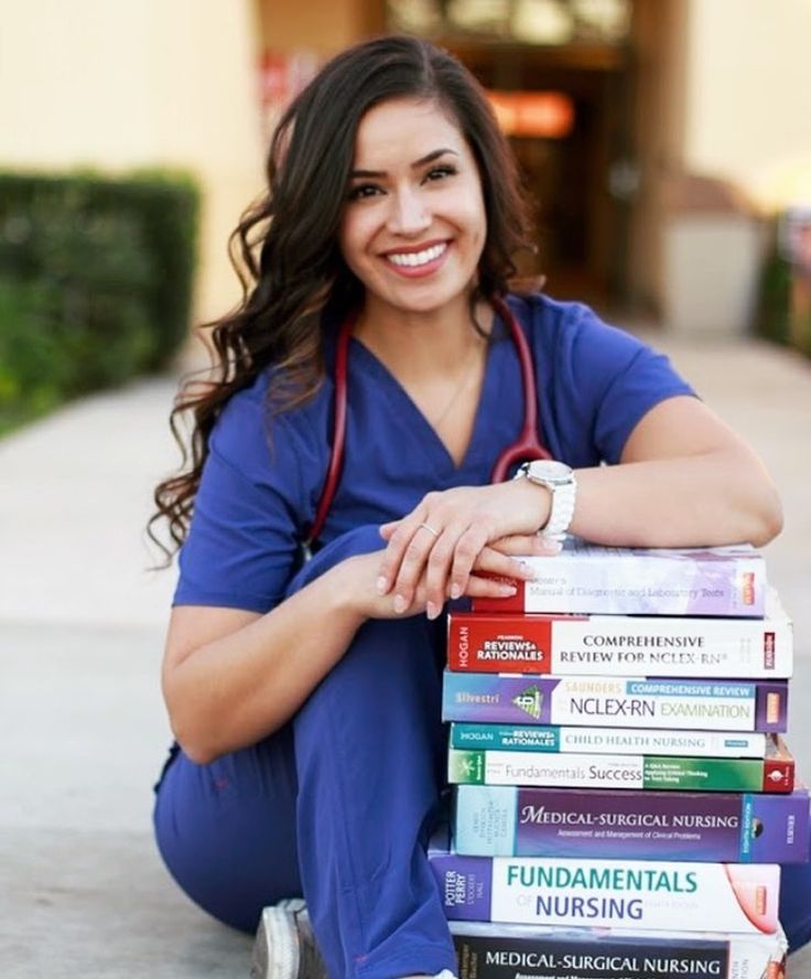 a woman in scrubs sitting on the ground with some books stacked on top of her