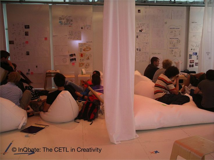 group of people sitting on bean bag chairs in an office with white walls and windows