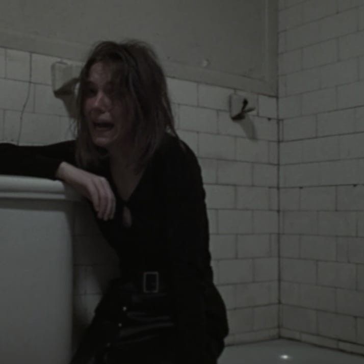 a woman sitting on the edge of a toilet in a room with white tile walls