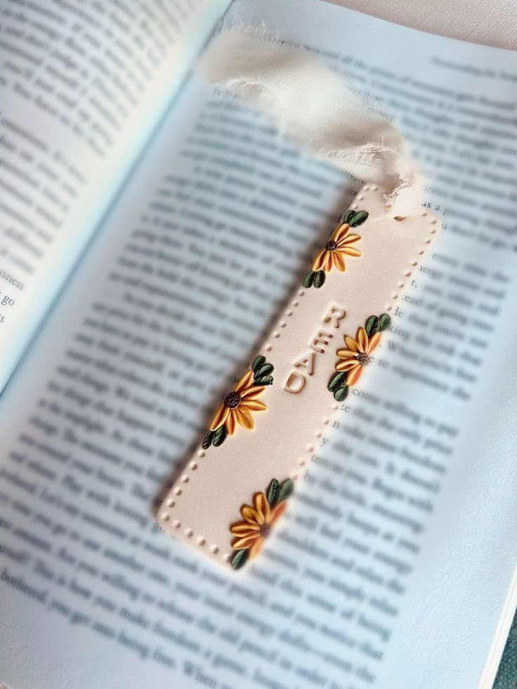 a bookmark with flowers on it sitting in front of an open book