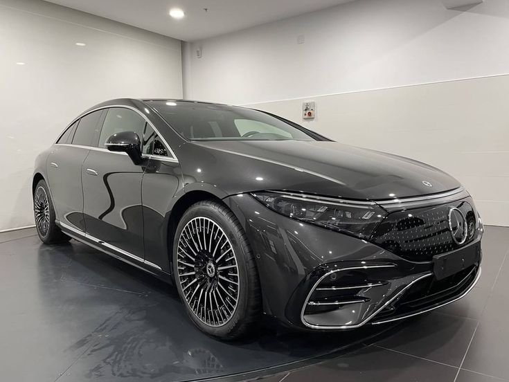 a grey car is parked in a large room with white walls and black flooring