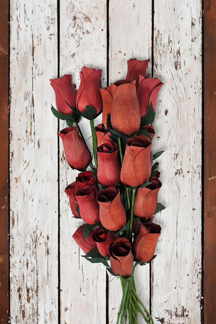 a bunch of red roses on a white wooden background with some green stems in the middle