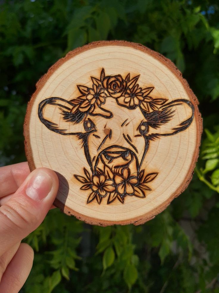 a person holding up a wooden cut out of a cow with flowers on it's head