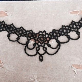 a black lace choker is laying on a white piece of fabric with holes in it