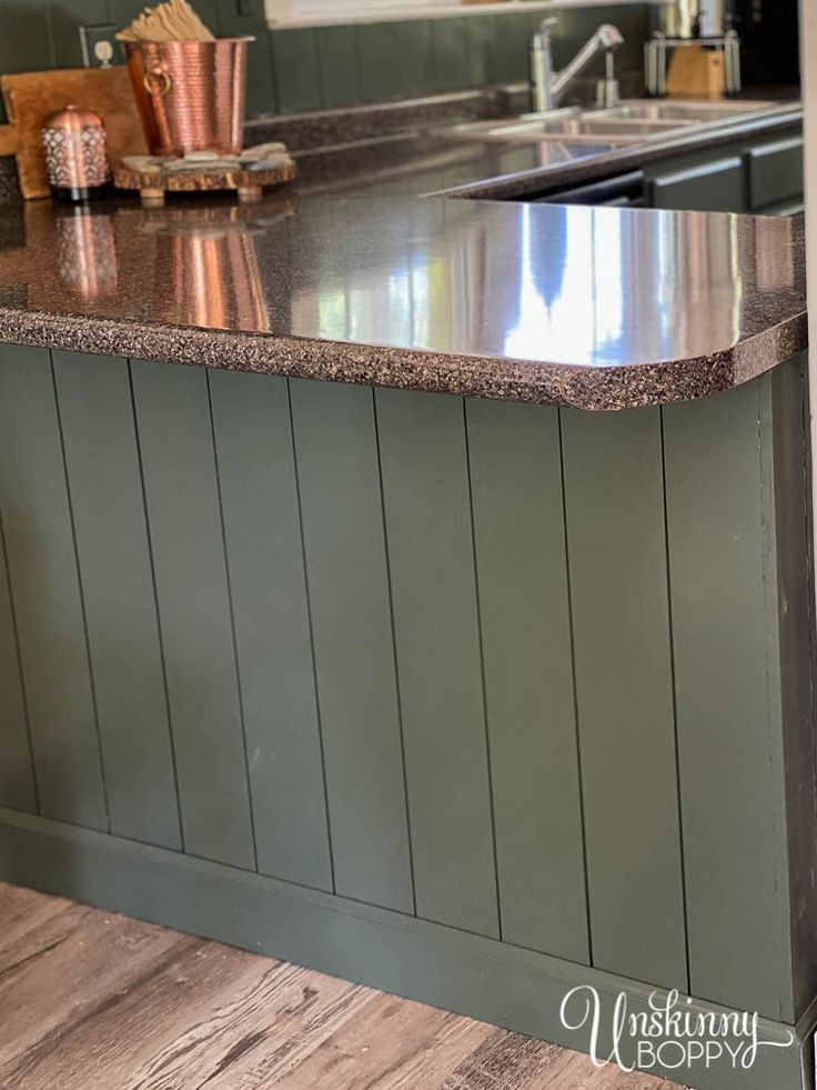 a kitchen with green painted cabinets and an island countertop in the center is a sink