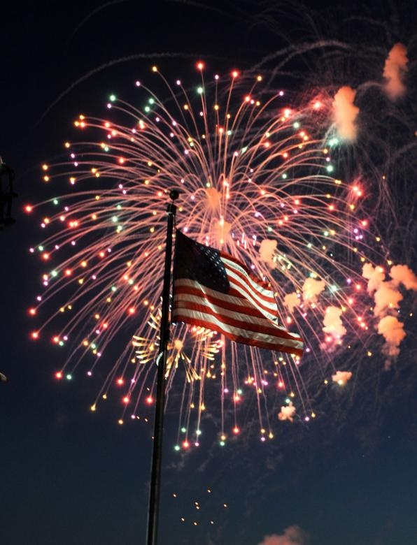 fireworks are lit up the night sky with an american flag on it's pole