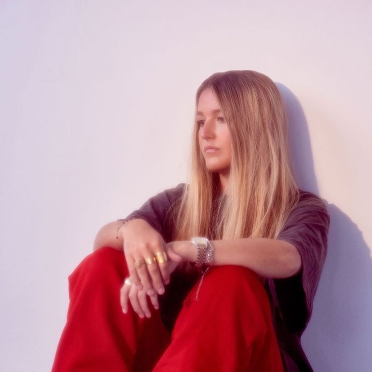 a woman sitting on the ground with her legs crossed, wearing red pants and a black shirt