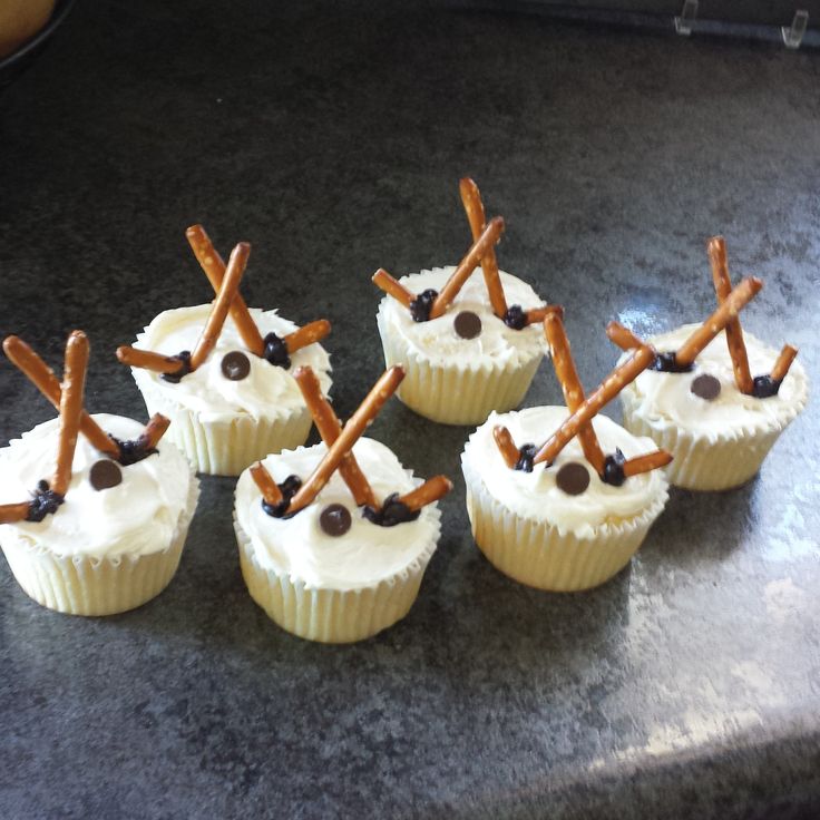 six cupcakes with white frosting and pretzel sticks sticking out of them