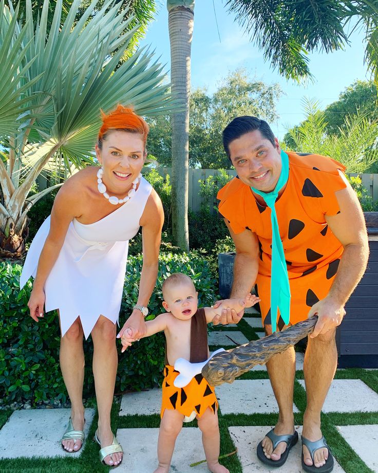 a man, woman and baby dressed up as flint the flintstones in front of a palm tree