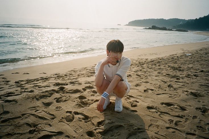 a young man sitting on top of a sandy beach next to the ocean