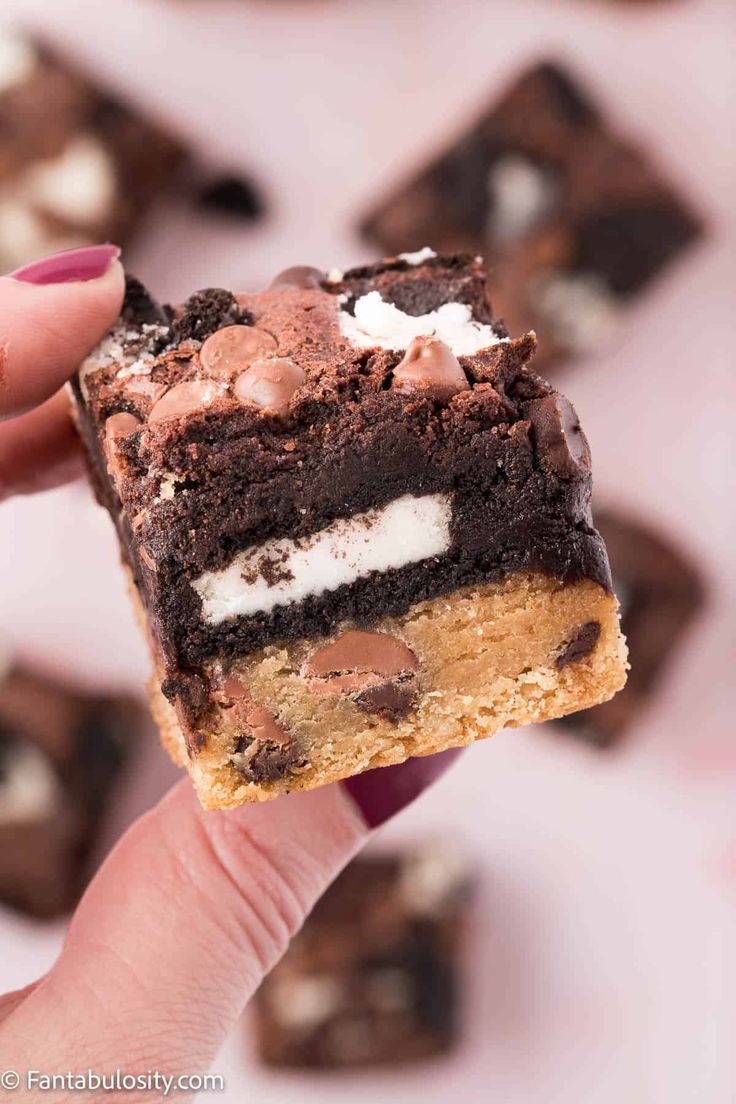 a hand holding a chocolate cookie bar with marshmallows on top and oreo cookies in the background