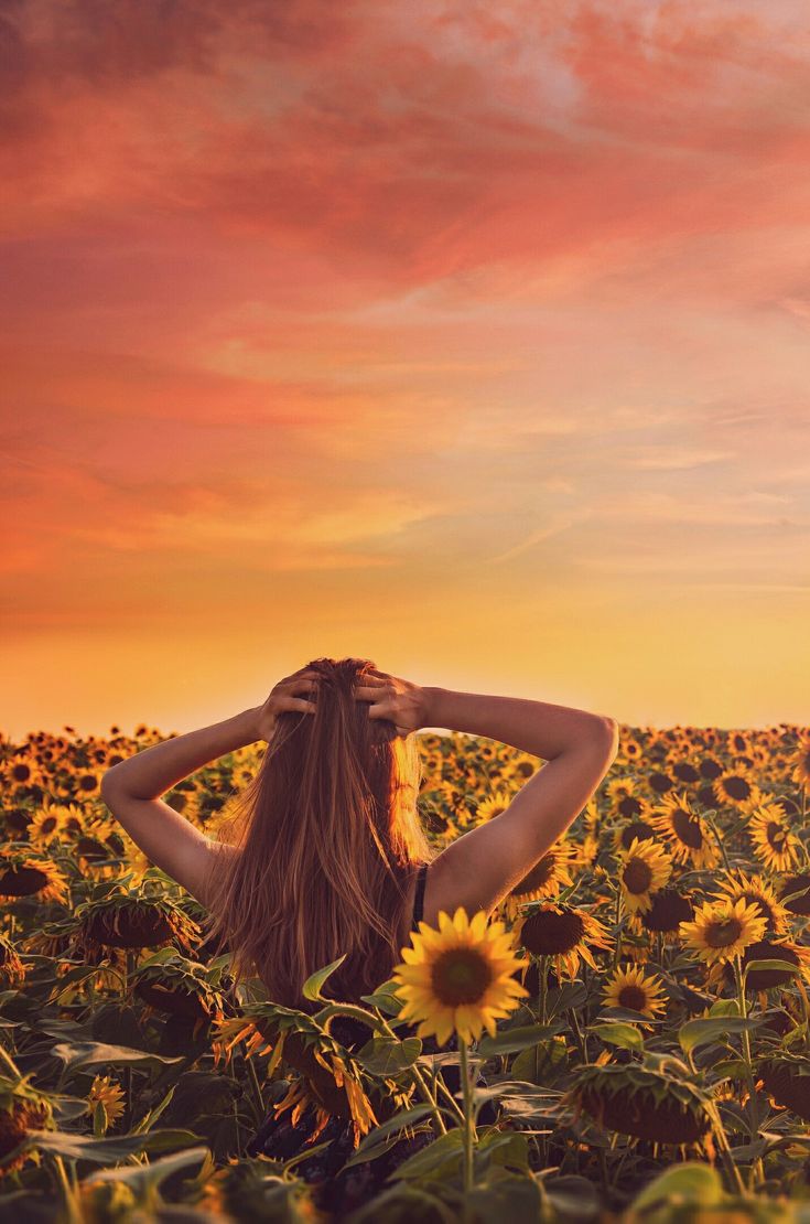 a woman standing in a field of sunflowers with her back to the camera