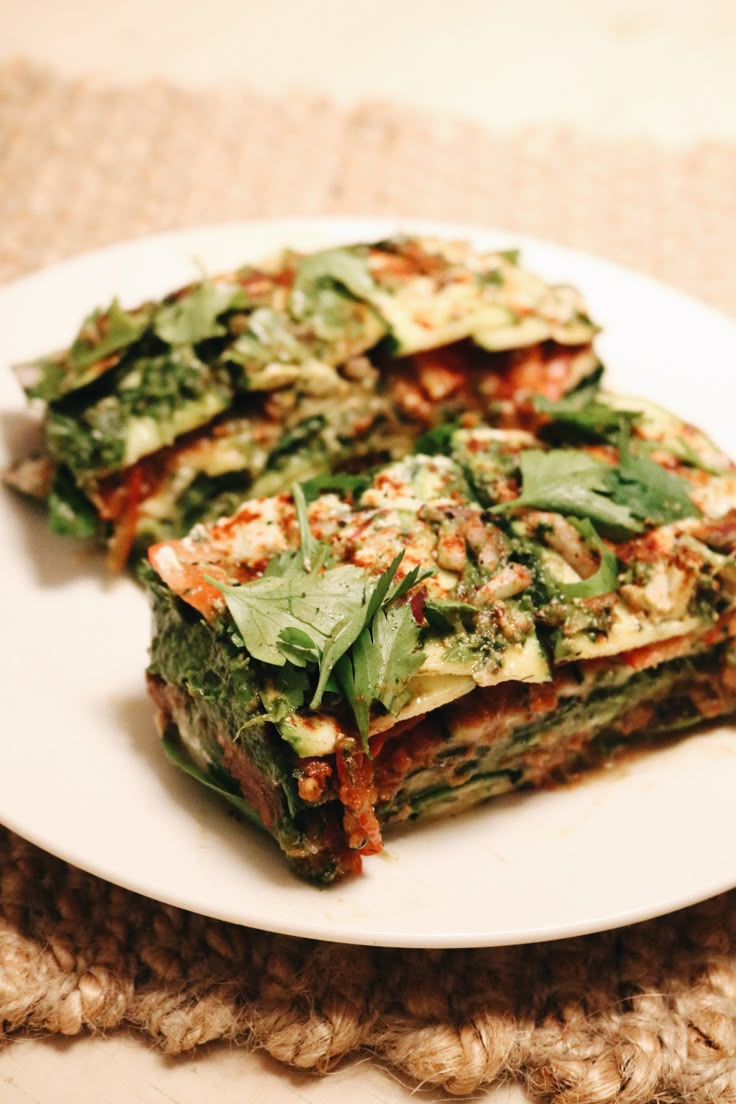 two slices of vegetable lasagna on a white plate with green leafy toppings