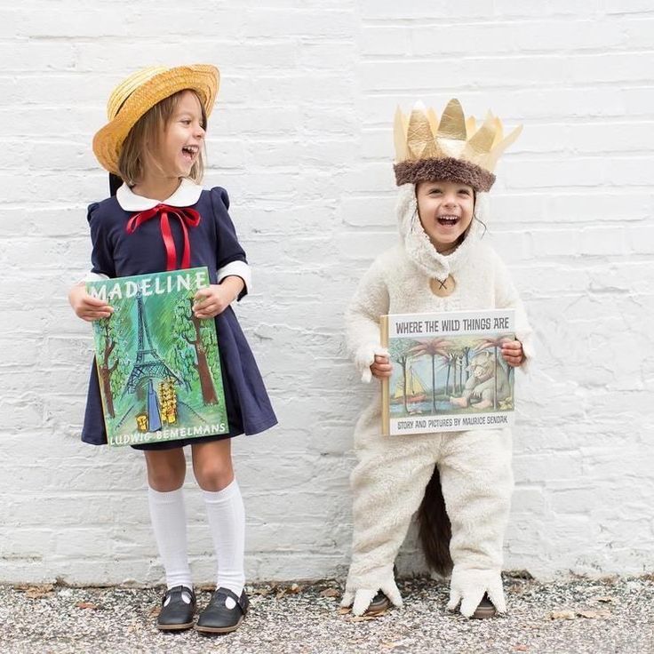 two children dressed in costumes standing next to each other and one is holding a newspaper