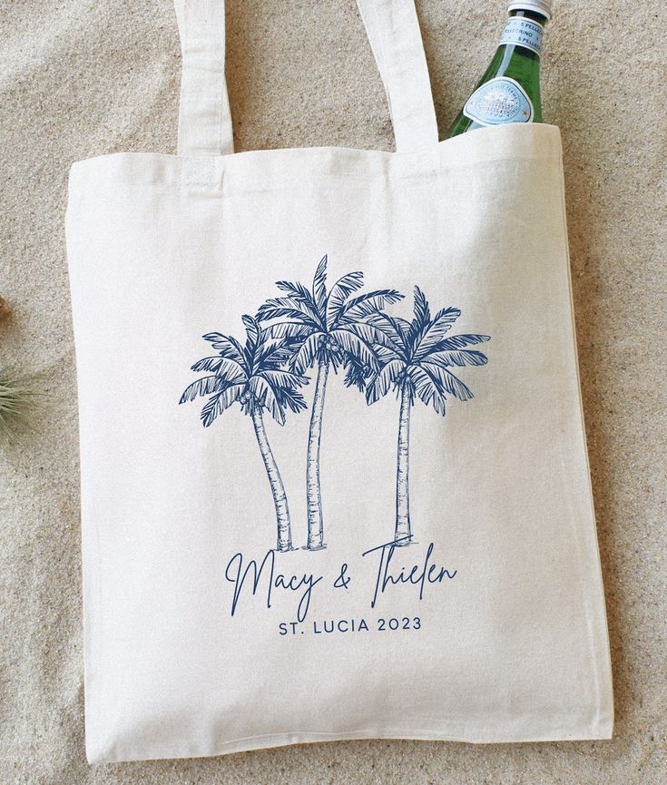 a tote bag with two palm trees on it and a bottle of beer next to it