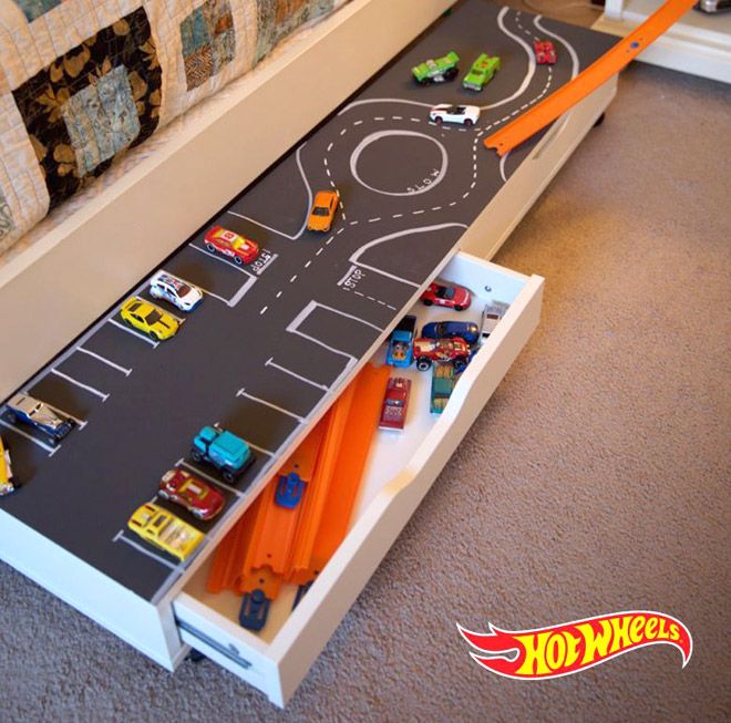 a toy car race track with cars and trucks on the floor next to a bed